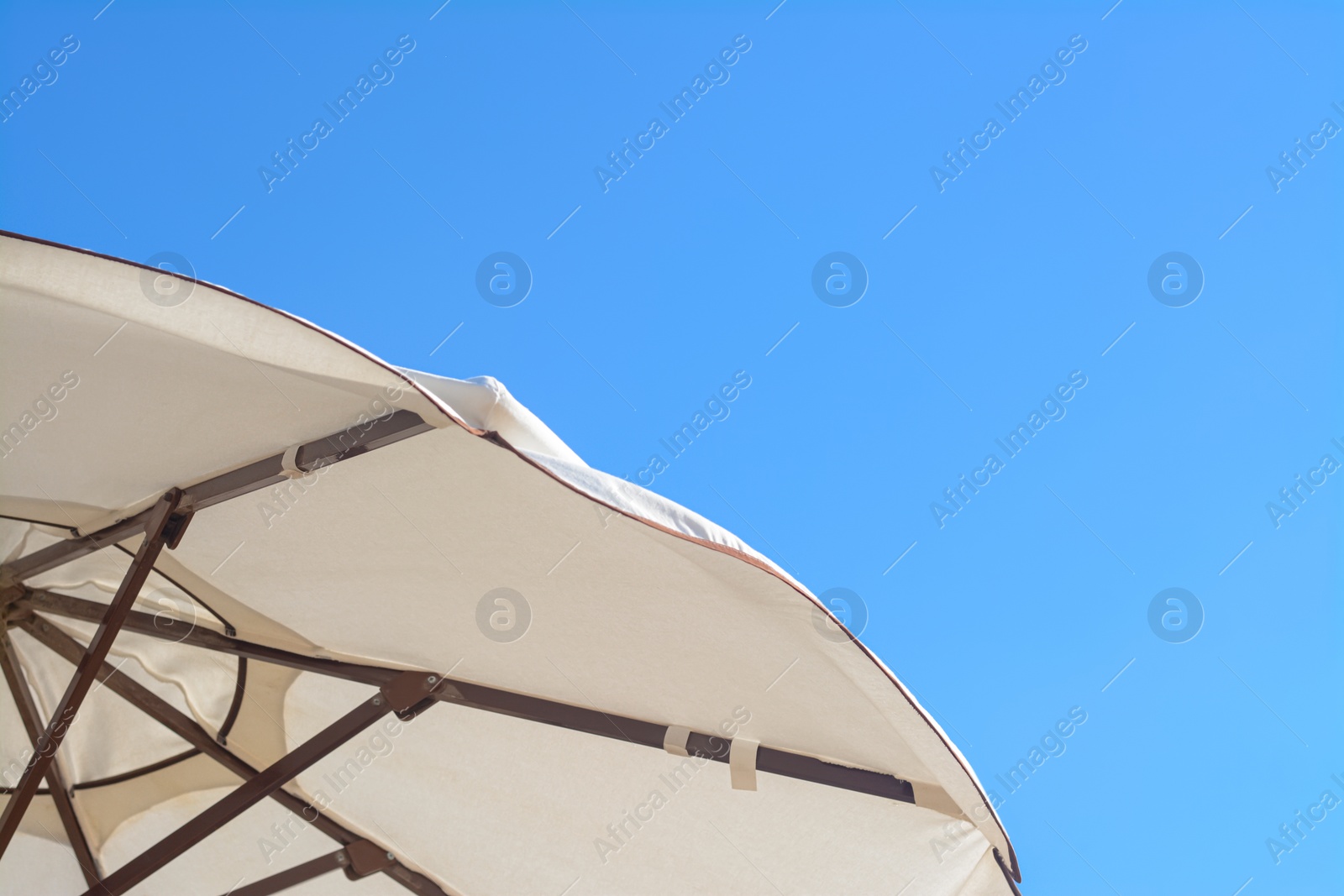 Photo of Beautiful white beach umbrella against blue sky, closeup. Space for text