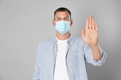 Photo of Man in protective mask showing stop gesture on grey background. Prevent spreading of coronavirus