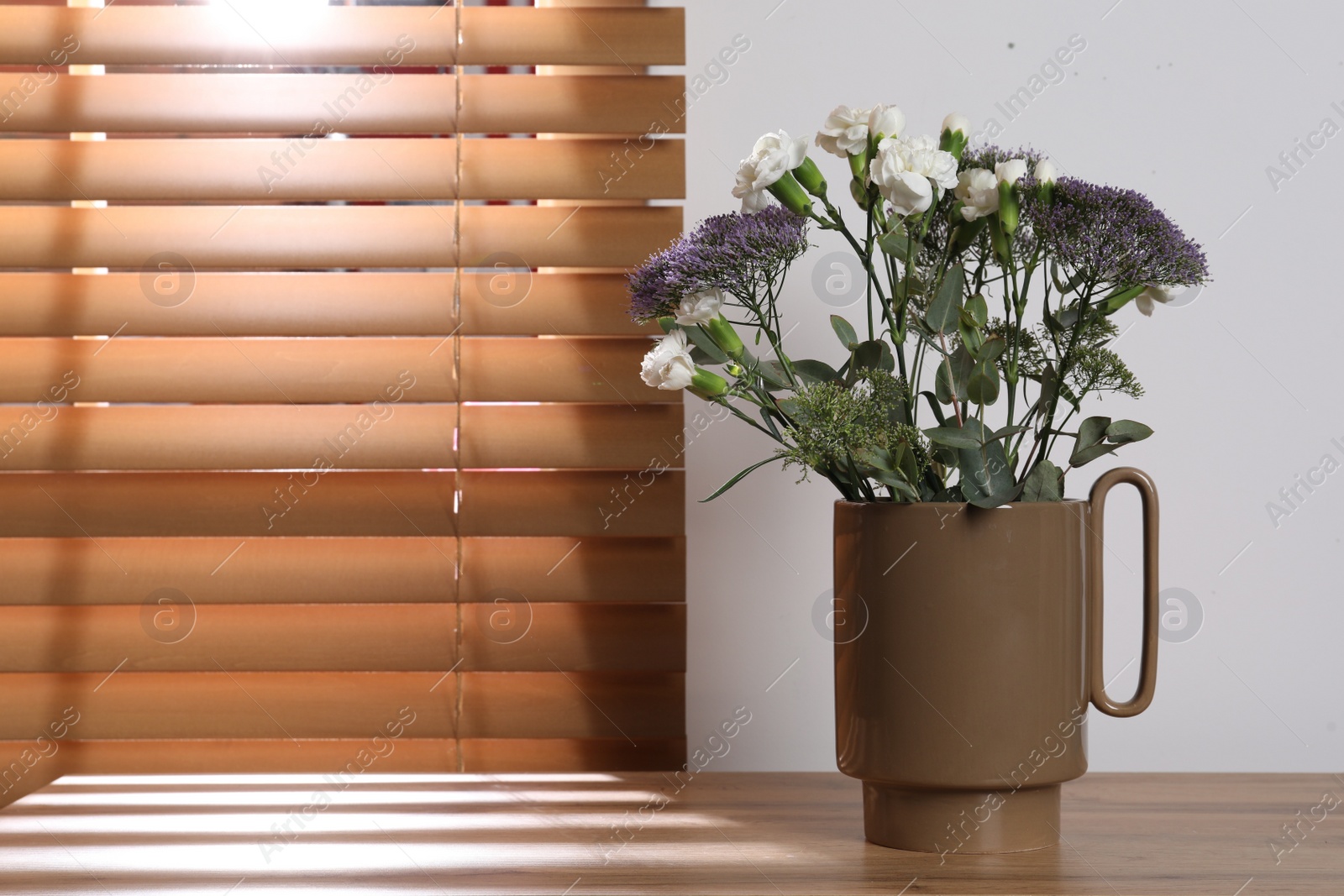 Photo of Stylish ceramic vase with beautiful flowers and eucalyptus branches on wooden table near window. Space for text