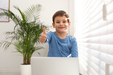 Happy little boy with modern laptop near window indoors