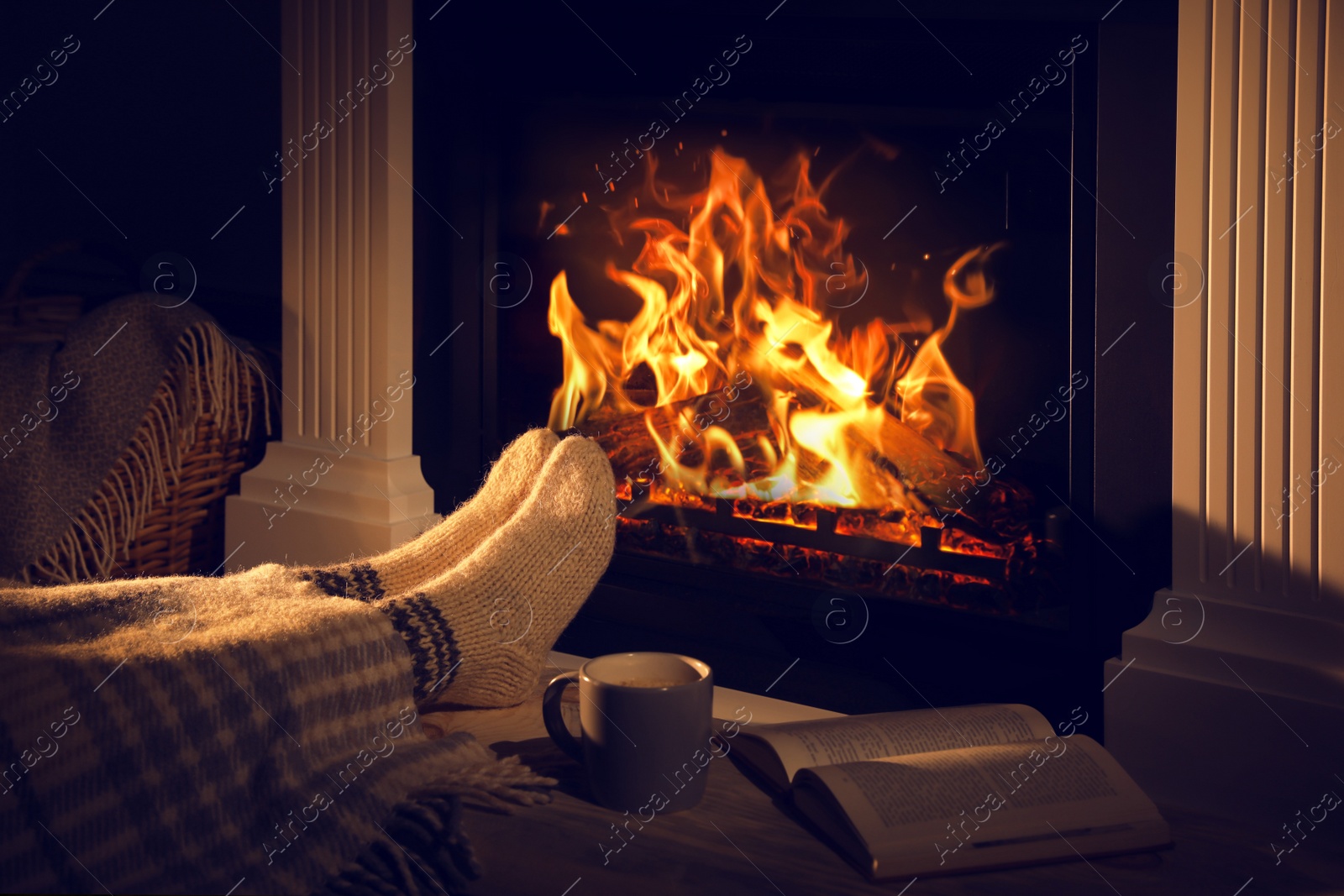 Photo of Woman with cup of drink and book near fireplace at home, closeup