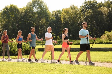 Photo of Group of people practicing Nordic walking with poles in park on sunny day