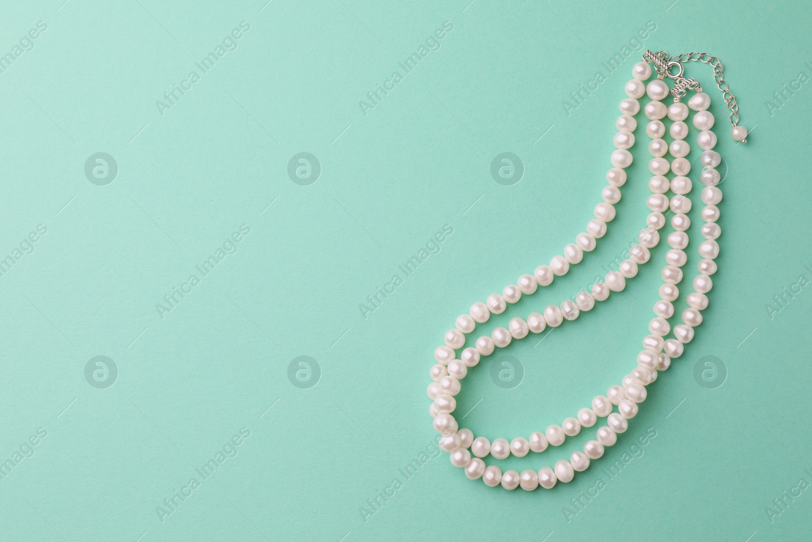 Photo of Elegant pearl necklace on turquoise background, top view. Space for text