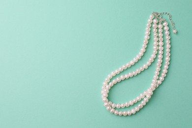 Elegant pearl necklace on turquoise background, top view. Space for text