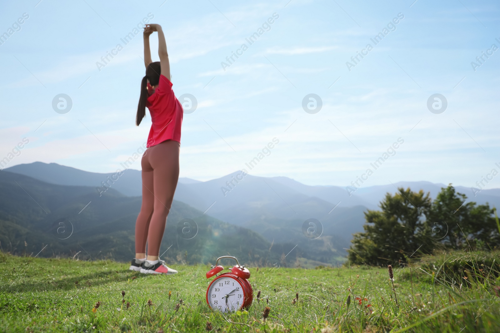 Photo of Woman doing morning exercise in mountains, focus on alarm clock