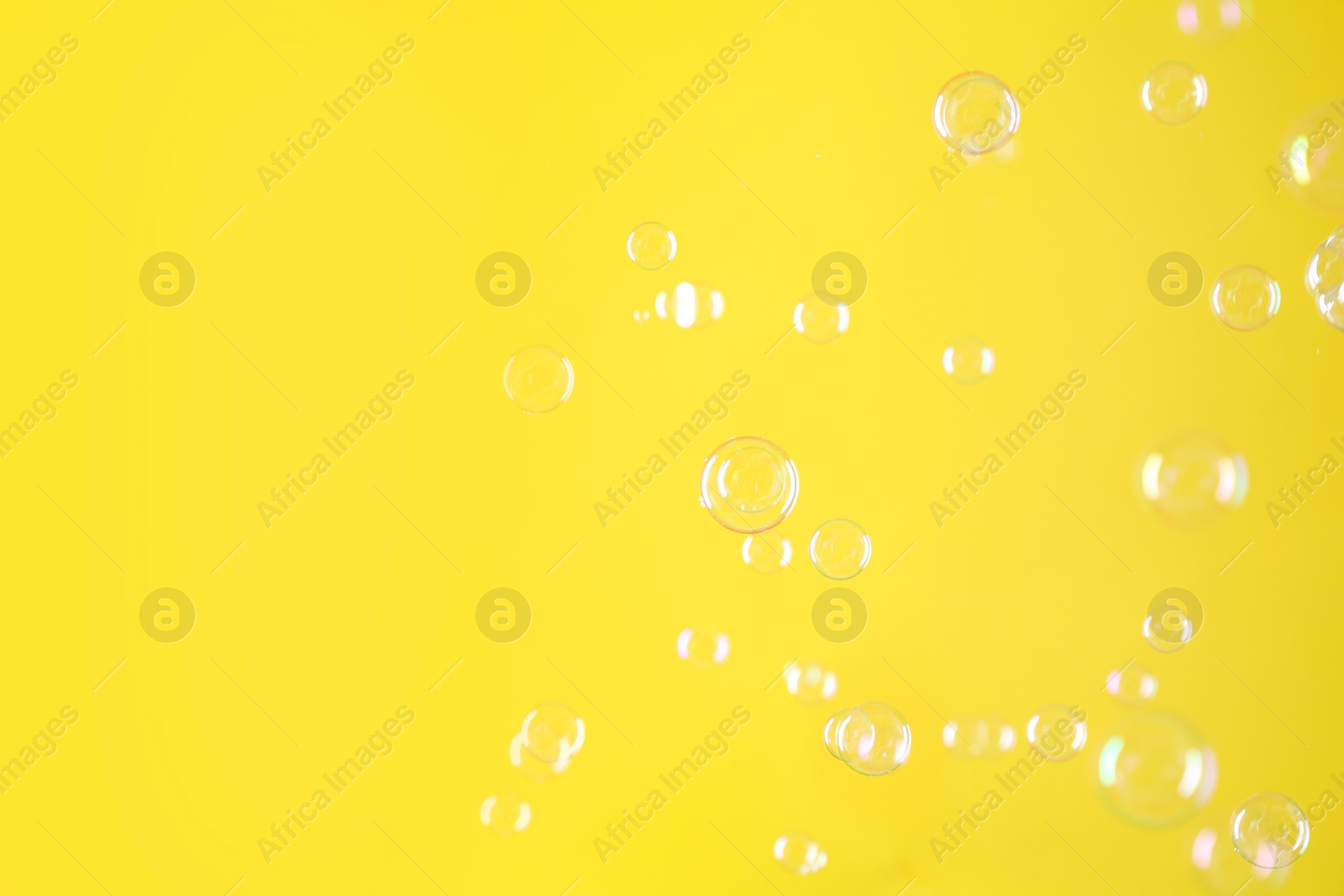 Photo of Beautiful transparent soap bubbles on yellow background, space for text