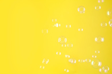 Photo of Beautiful transparent soap bubbles on yellow background, space for text