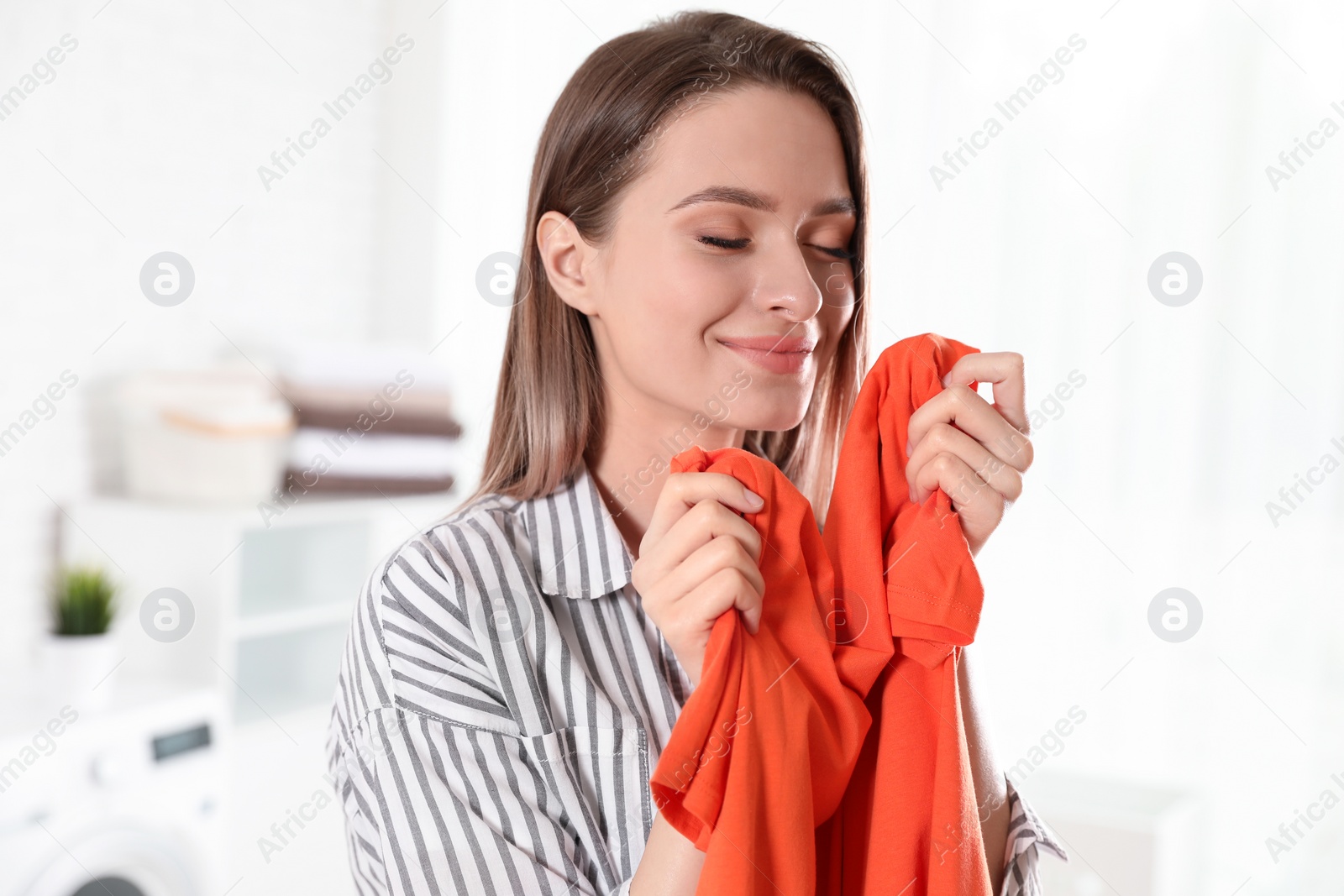 Photo of Happy young woman with clean t-shirt indoors. Laundry day