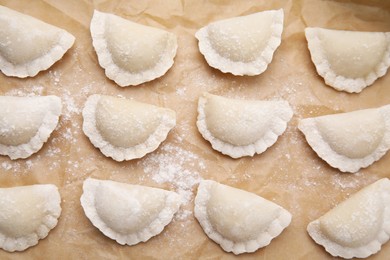 Photo of Raw dumplings (varenyky) with tasty filling and flour on parchment paper, flat lay