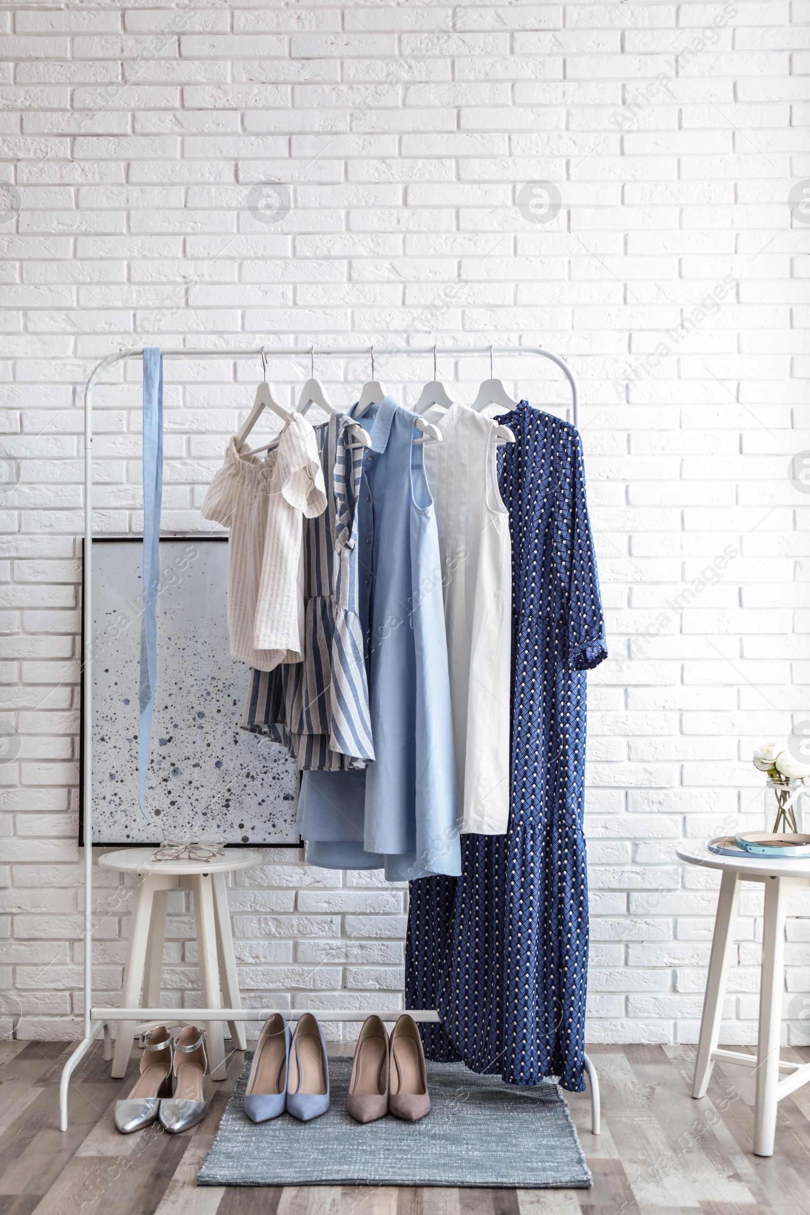 Photo of Wardrobe rack with women's clothes and different shoes at white brick wall in room