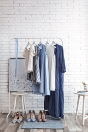 Photo of Wardrobe rack with women's clothes and different shoes at white brick wall in room