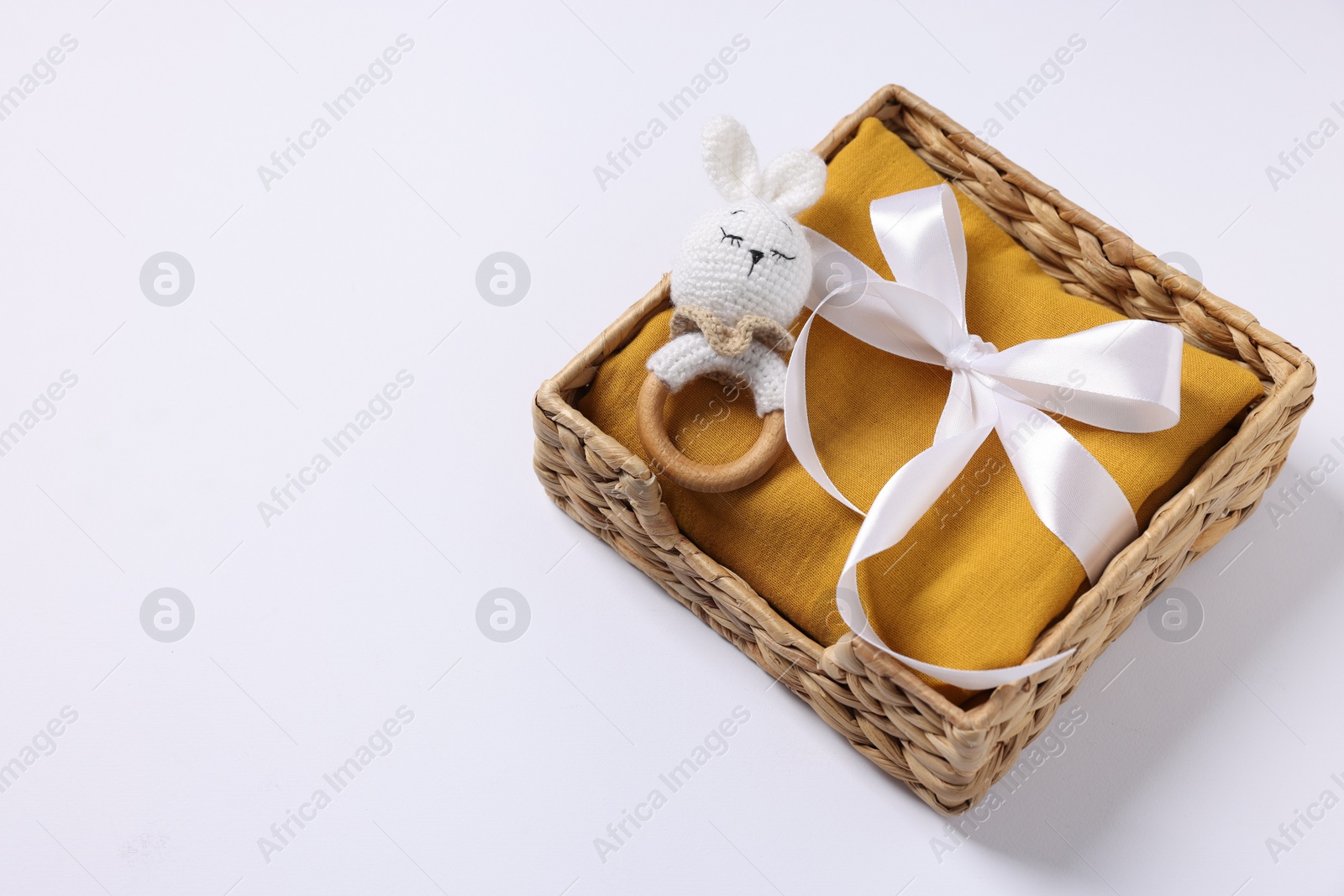 Photo of Baby accessory. Rattle and child`s clothes in wicker box on white background. Space for text