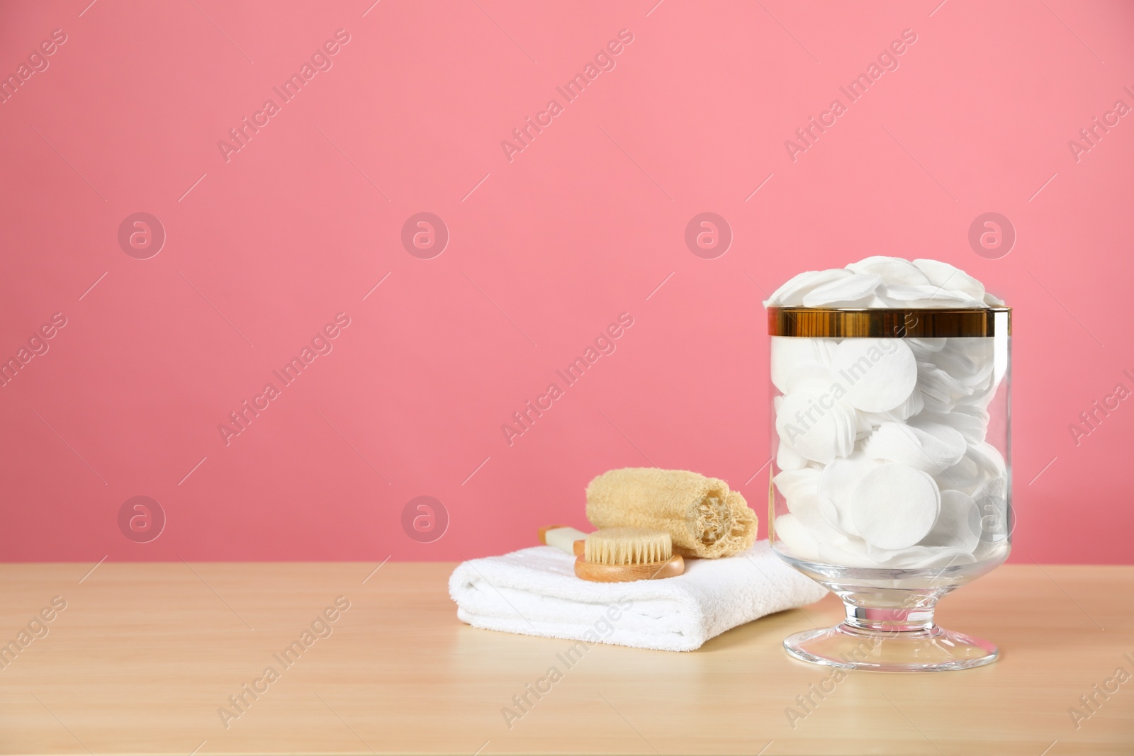 Photo of Jar with cotton pads on wooden table against pink background. Space for text