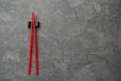 Photo of Pair of red chopsticks with rest on grey table, top view. Space for text