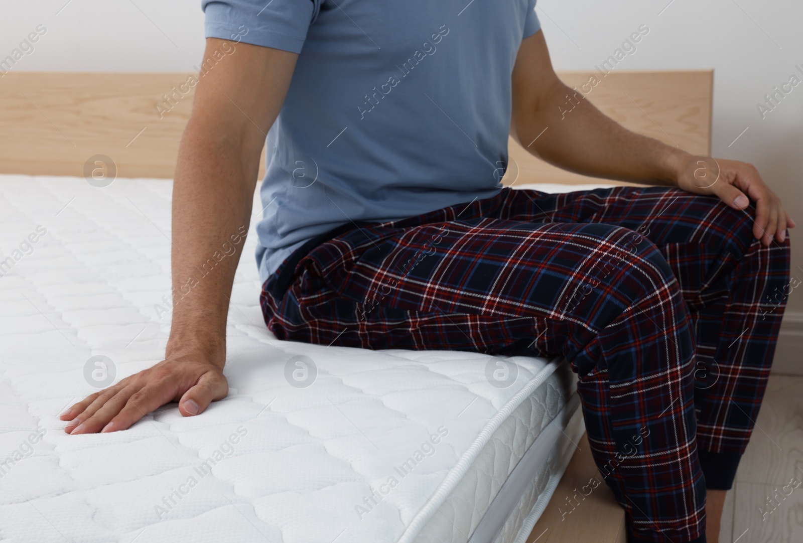 Photo of Man sitting on bed with comfortable mattress at home, closeup