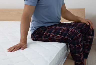 Photo of Man sitting on bed with comfortable mattress at home, closeup