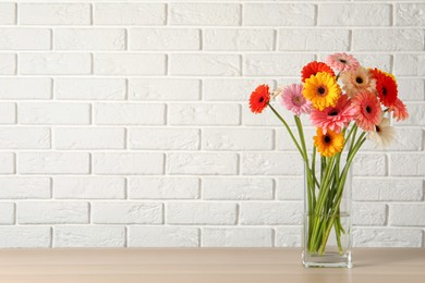 Photo of Bouquet of beautiful colorful gerbera flowers in vase on table against white brick wall. Space for text
