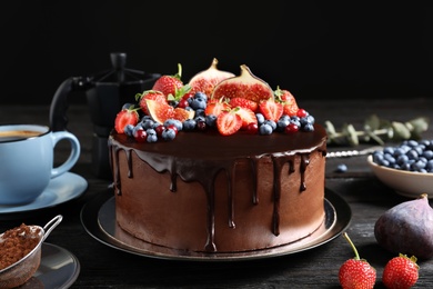 Fresh delicious homemade chocolate cake with berries on table against dark background