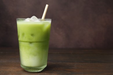 Glass of tasty iced matcha latte on wooden table. Space for text