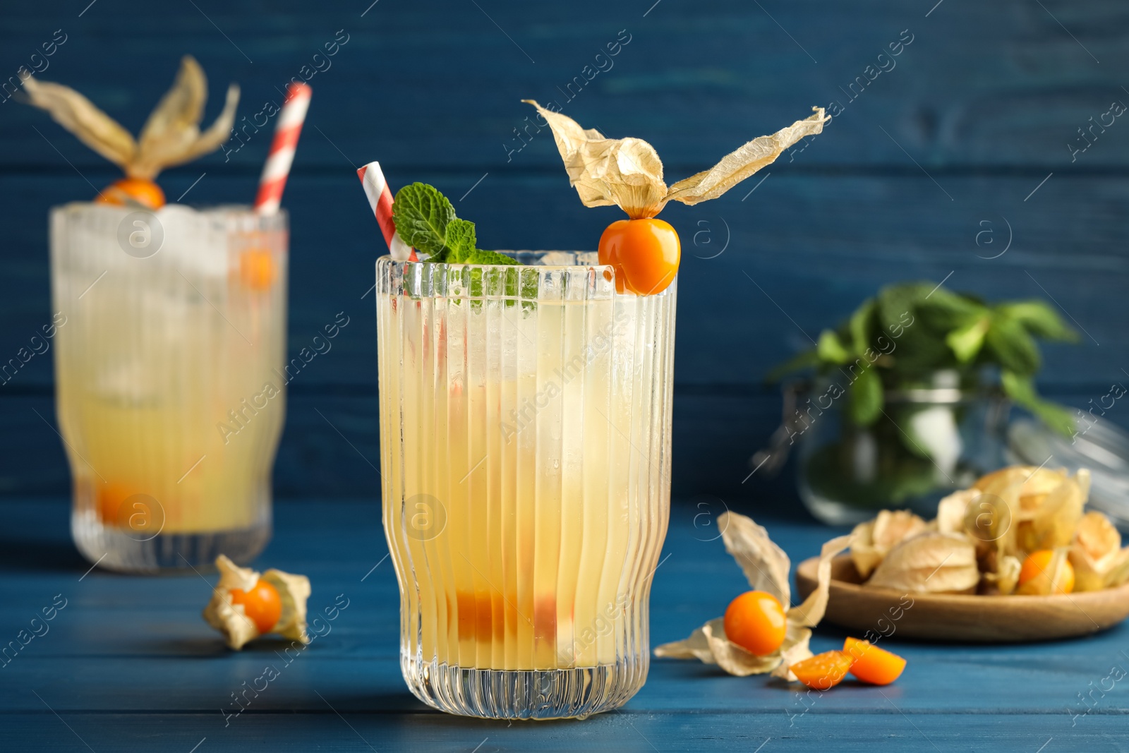 Photo of Refreshing cocktail decorated with physalis fruit on blue wooden table