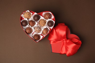 Photo of Heart shaped box with delicious chocolate candies on brown background, flat lay
