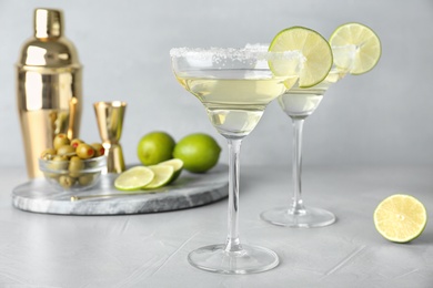 Photo of Glasses of lemon drop martini cocktail with lime slice on light table against grey background
