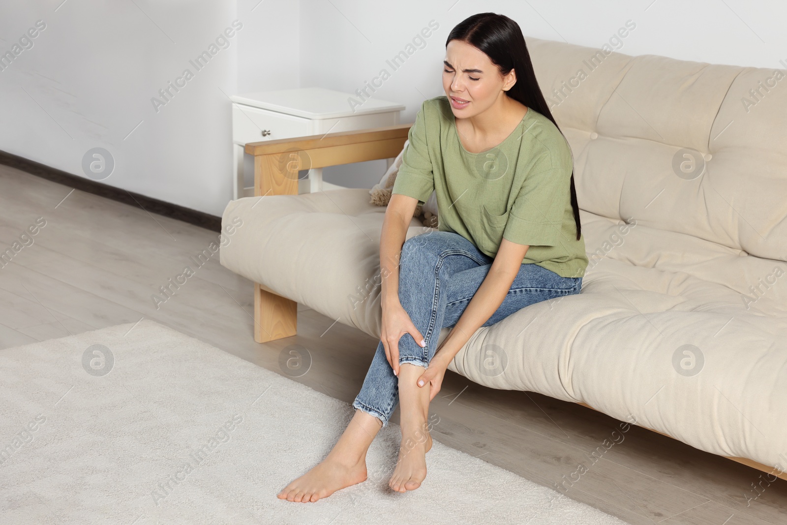 Photo of Woman rubbing sore leg on sofa at home