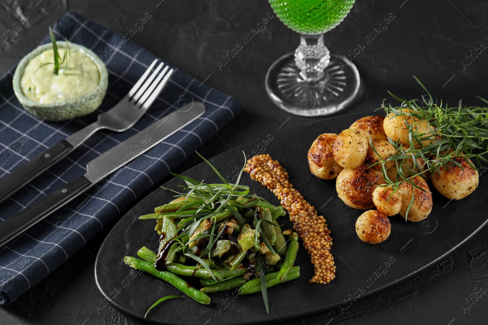 Photo of Delicious salad with tarragon, mustard and grilled potatoes served on black textured table