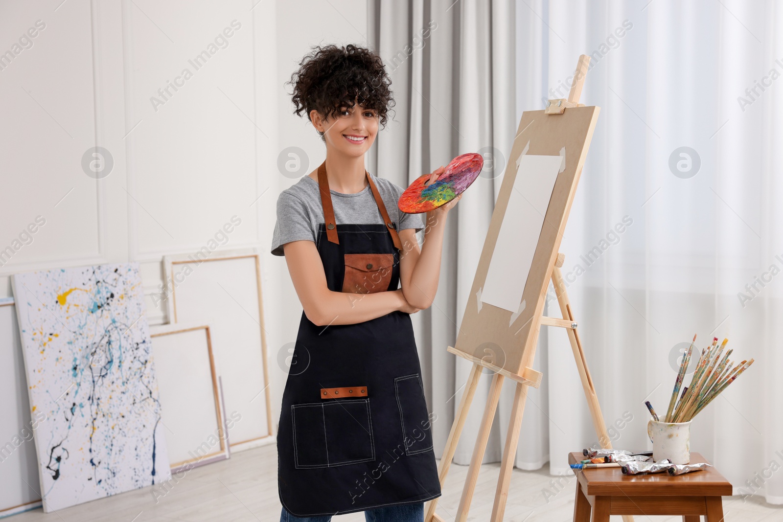 Photo of Young woman with palette near easel in studio