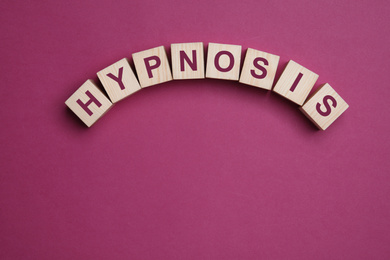 Photo of Wooden blocks with word HYPNOSIS on magenta background, flat lay