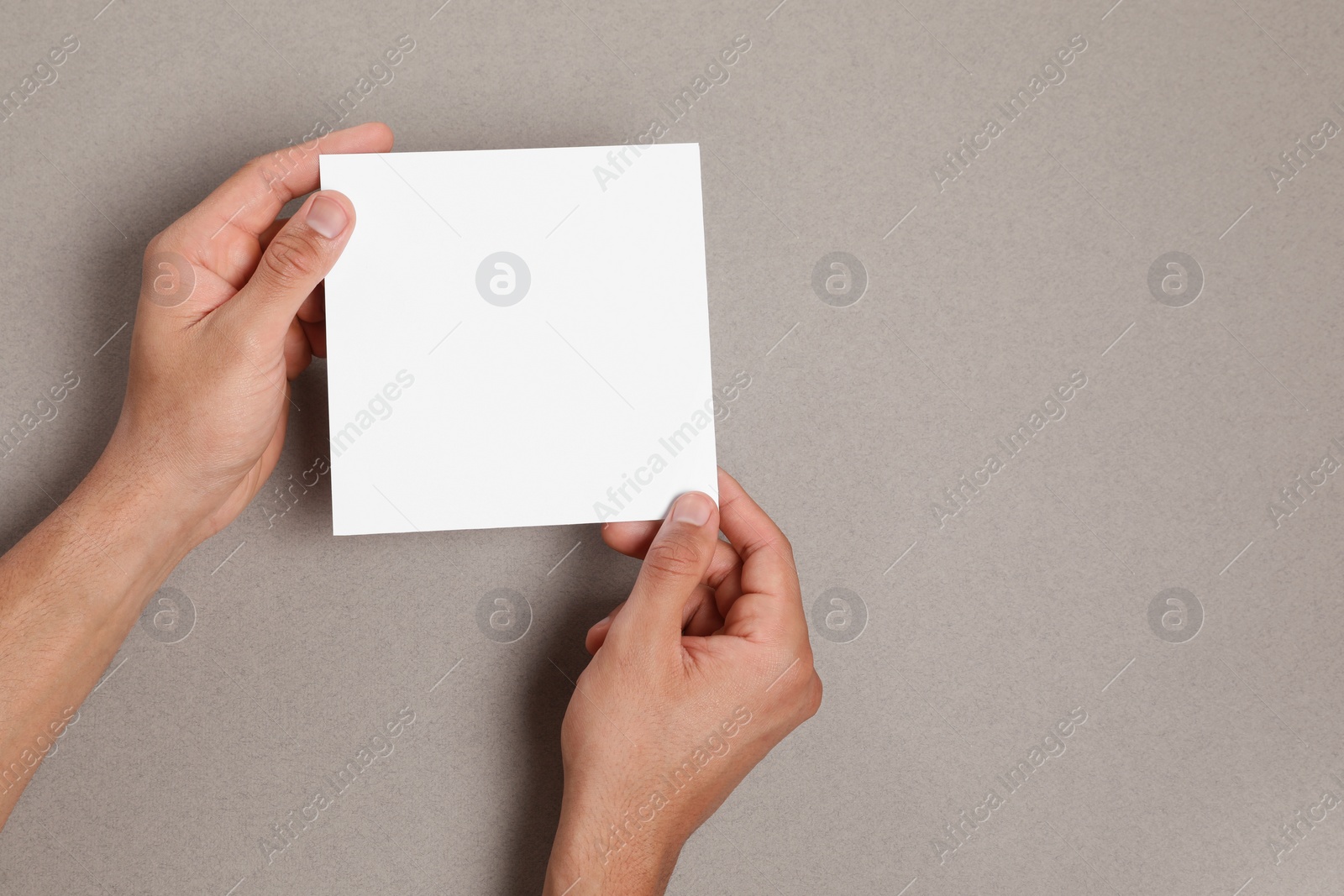 Photo of Man holding sheet of paper on grey background, closeup. Mockup for design