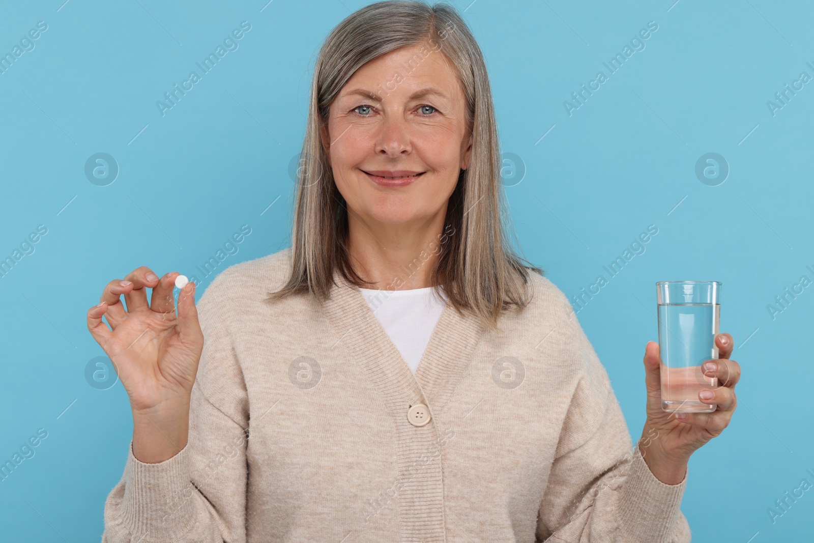 Photo of Senior woman with glass of water and pill on light blue background