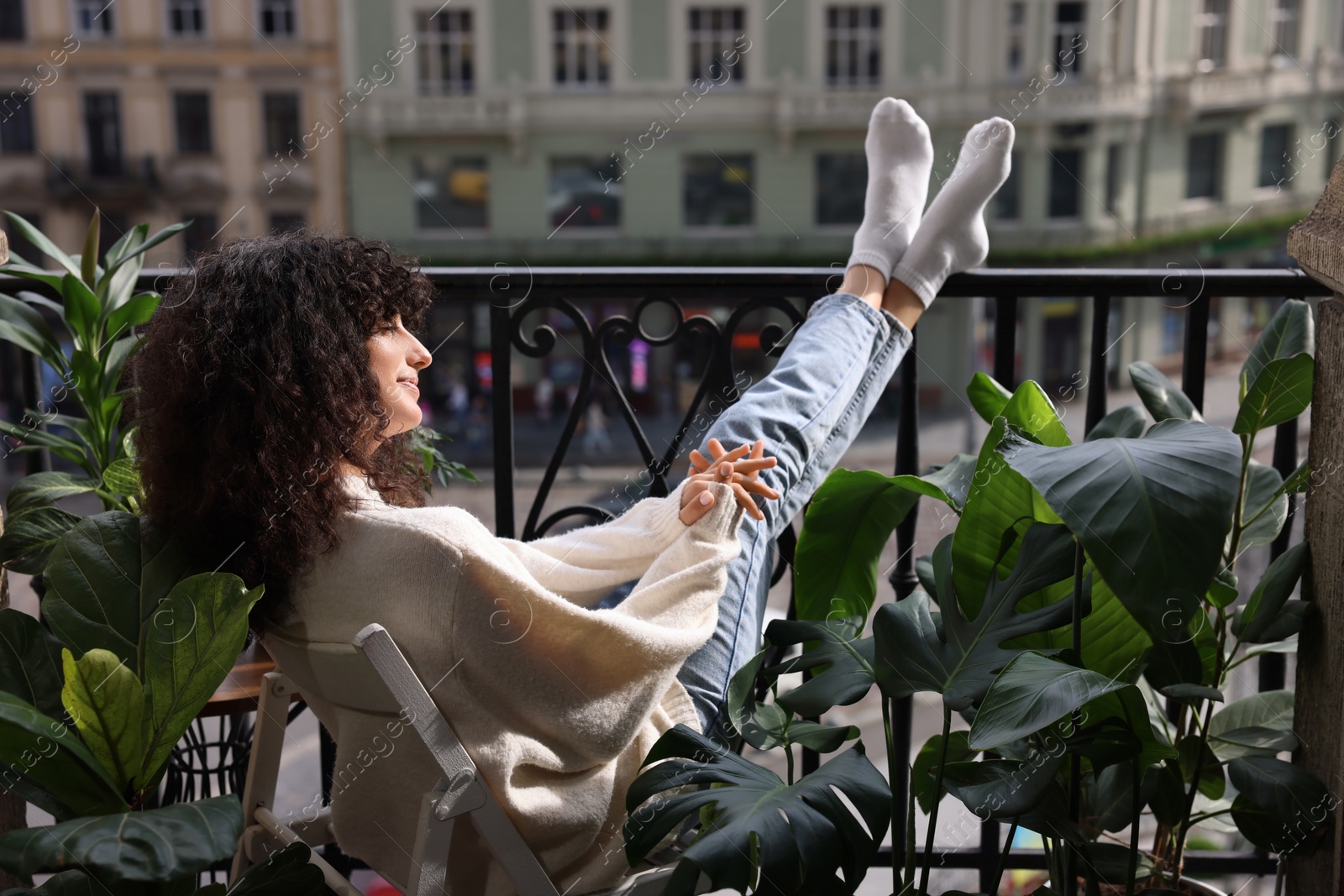 Photo of Beautiful young woman relaxing in chair surrounded by green houseplants on balcony