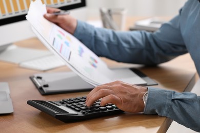 Photo of Professional accountant using calculator at wooden desk, closeup