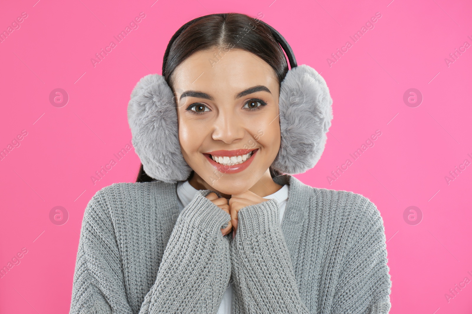 Photo of Beautiful young woman wearing earmuffs on pink background