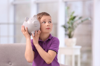 Photo of Little boy with piggy bank at home