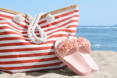 Photo of Stylish striped bag with slippers on sandy beach near sea, closeup