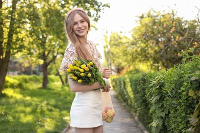 Photo of Beautiful teenage girl with bouquet of yellow tulips and apples in park on sunny day