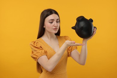 Sad woman with piggy bank on orange background