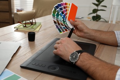 Professional designer with graphic tablet at wooden table, closeup