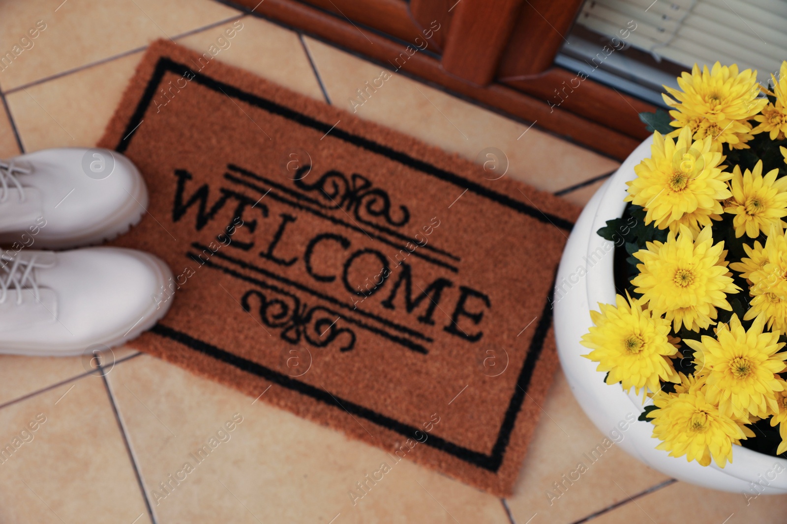 Photo of Door mat with word Welcome, stylish boots and beautiful flowers on floor, above view