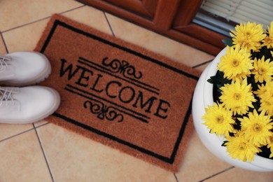 Photo of Door mat with word Welcome, stylish boots and beautiful flowers on floor, above view