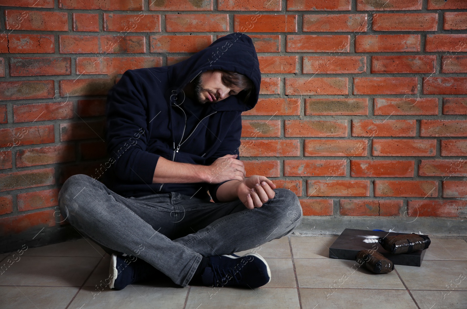 Photo of Young addicted man sitting near brick wall after using drugs. Space for text