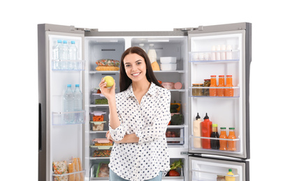 Young woman with apple near open refrigerator on white background