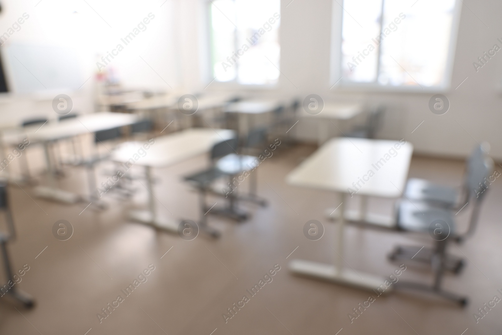 Photo of Blurred view of empty school classroom with desks, windows and chairs