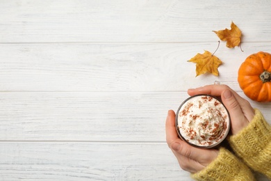 Woman holding tasty pumpkin latte at white wooden table, top view. Space for text