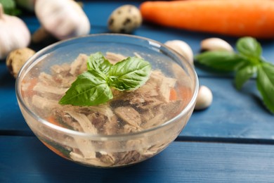 Photo of Delicious aspic with meat in bowl on blue wooden table, closeup