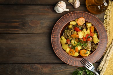 Photo of Tasty cooked dish with potatoes in earthenware served on wooden table, flat lay. Space for text