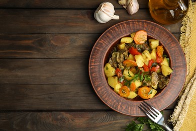 Tasty cooked dish with potatoes in earthenware served on wooden table, flat lay. Space for text