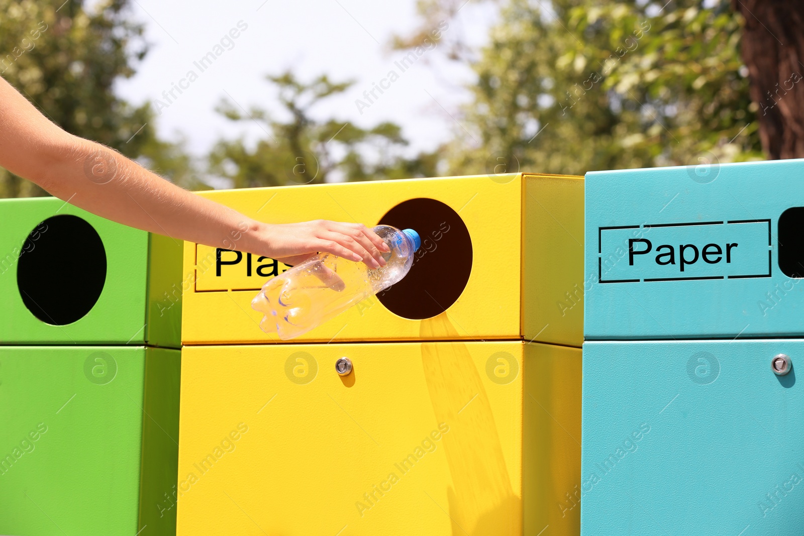 Photo of Woman throwing plastic bottle into sorting bin on city street, closeup. Recycling waste